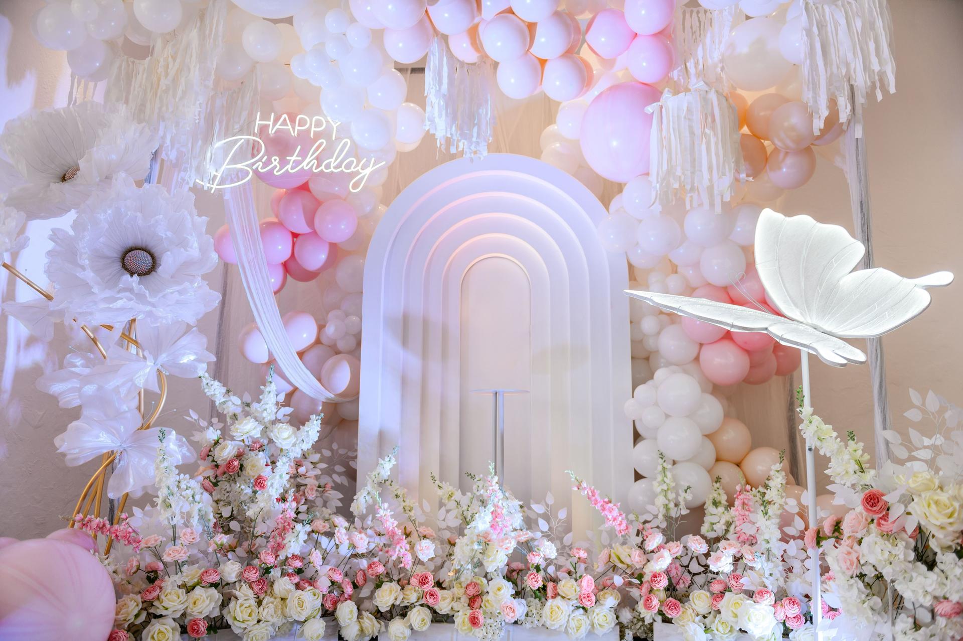 Birthday party for baby girl on a background photo wall. Arch decoration pink, white balloons, text Happy Birthday, flowers, paper decor butterfly. Children's photo zone.